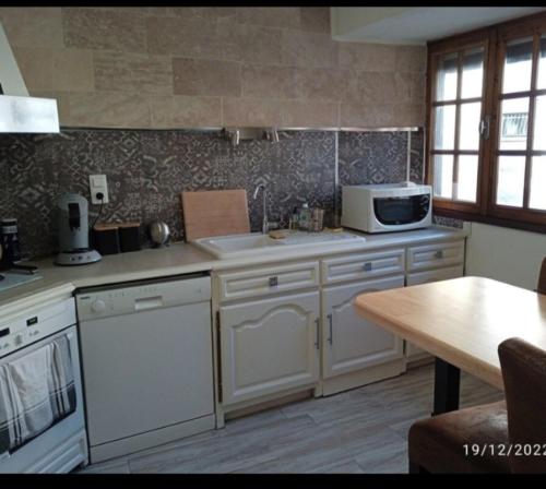 a kitchen with white cabinets and a microwave and a table at Maison village en Aveyron in Durenque