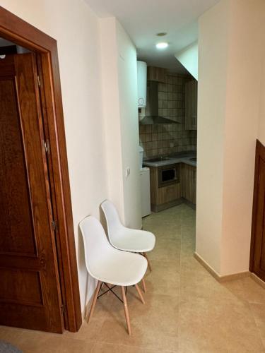 two white chairs in a room with a kitchen at Apartamentos Peñaflor in Guadix