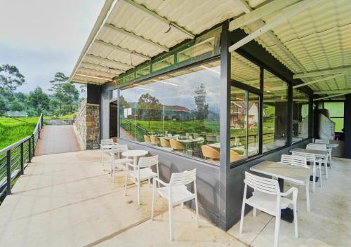 a patio with white chairs and tables and windows at AJ Gable Clouds Ooty by VOYE HOMES - Serene Stay Near Avalanche Emerald Lake in Ooty