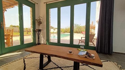 a living room with a wooden table and large windows at WINK house : Charme et Sérénité in Essaouira