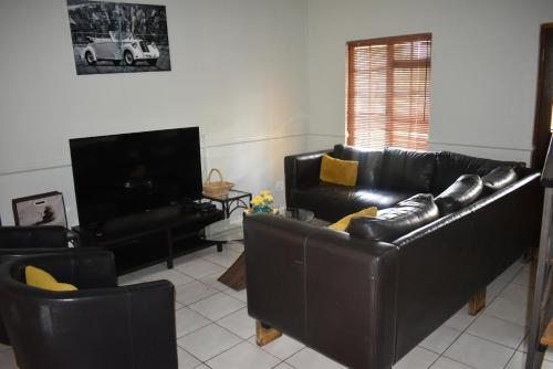 a living room with black leather furniture and a flat screen tv at Pendleberry Grove Holidays in Bela-Bela