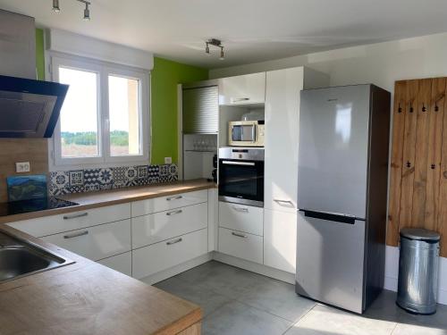 une cuisine avec des armoires blanches et un réfrigérateur en acier inoxydable dans l'établissement Maison de campagne, à Beuzeville-la-Guérard