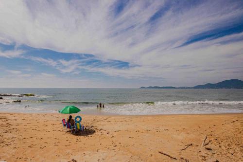 two people sitting under an umbrella on a beach at Casa com lareira e a 450 metros da praia QZ7460 in Penha