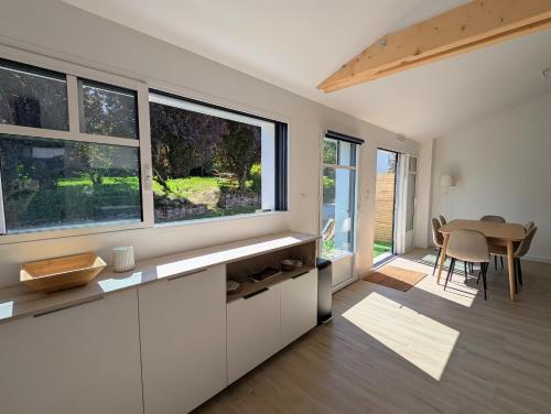 une cuisine avec des placards blancs, une table et des fenêtres dans l'établissement Havre de paix Maison rénovée avec jardin, à Pornic