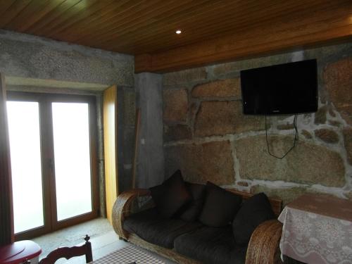 a living room with a couch and a tv on a stone wall at Casa da Bôcha in Cativelos