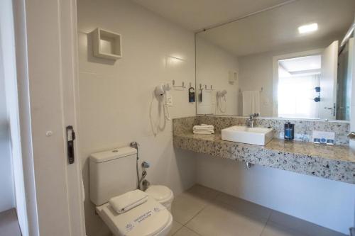 a bathroom with a toilet and a sink and a mirror at Hotel VillaReal Guaratuba - Caieiras in Guaratuba