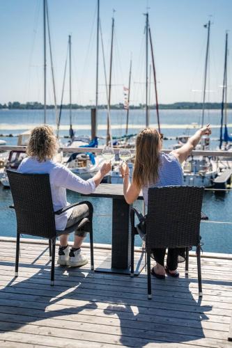 two people sitting at a table on a dock with boats at Hausboot ELLA- Huus & Meer in Burgstaaken