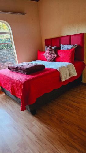 a bedroom with a large bed with red sheets and pillows at Happy Stay Guest House Mafikeng in Mahikeng