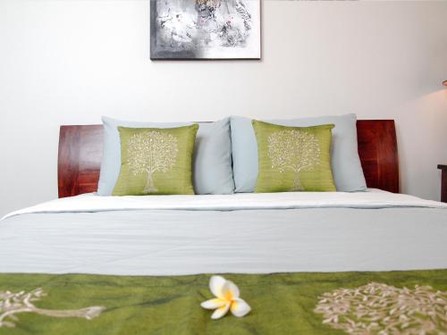 a white bed with green pillows and a flower on it at Linda Villa Sanur in Sanur