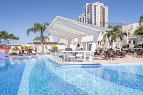a swimming pool with a white canopy next to a building at Apto Vista Mar Home Club Pé na Areia 3 Quartos Ares Condicionados Cozinha Completa Piscina Aquecida Jacuzzi Sauna Academia Quadra Playground Salão de Jogos 15min do Beto Carrero in Piçarras