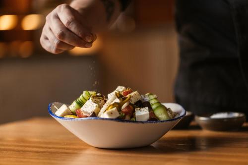 a person sprinkling food in a bowl on a table at Cook's Club Ialysos Rhodes in Ialyssos
