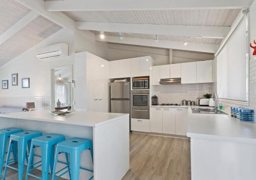 a white kitchen with white cabinets and blue stools at Seaesta Rye by Ready Set Stay - BYO LINEN & TOWELS in Rye