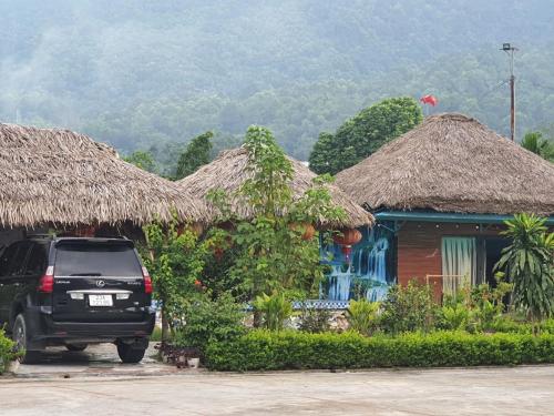 a car parked in front of a house with thatched roofs at Ha Giang Eco Bungalow in Ha Giang