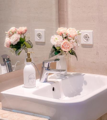 a bathroom sink with a bottle of soap and flowers at Gold Coast PIK Apartments by Host Jess in Jakarta