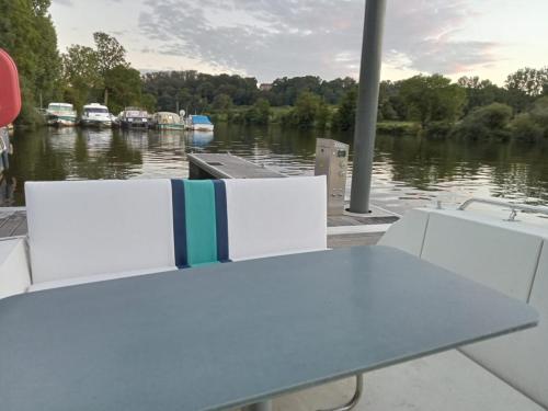une table et des chaises sur un bateau sur une rivière dans l'établissement Bateau-gîte sur le halage de la Mayenne, à LʼHuisserie