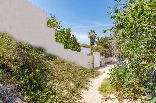 a path next to a white wall with a palm tree at Villa Kareema 2D con accesso diretto alla Spiaggia di San Pietro in Bevagna in San Pietro in Bevagna