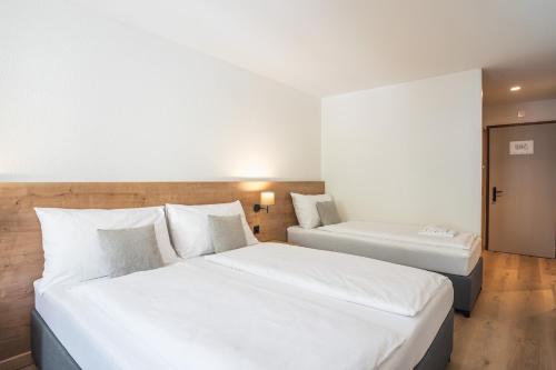 two beds in a hotel room with white sheets at Hotel Brocco & Posta in San Bernardino