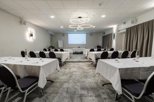a conference room with white tables and chairs and a screen at The Originals Boutique, Hôtel Le Pariou, Issoire in Issoire