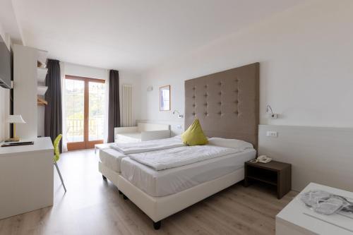 a white bedroom with a large bed with a yellow pillow at Park Hotel Val Di Monte ***S in Malcesine