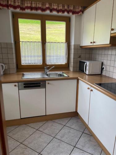 a kitchen with white cabinets and a sink and a microwave at Residence Bondì in Colfosco