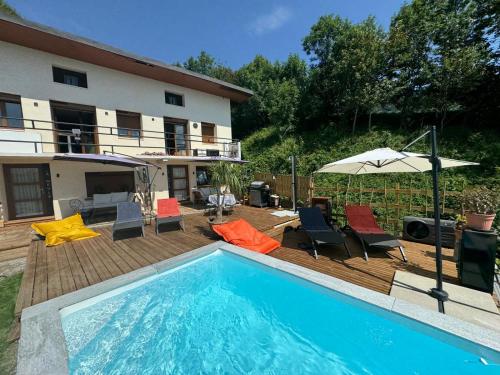a swimming pool with chairs and an umbrella next to a house at LE MOULIN DE NAVETTE - La Meule in Aigueblanche