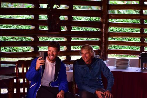 two men sitting at a table looking at a cell phone at Kibale Guest Cottages in Fort Portal
