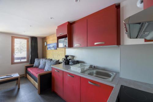 une petite cuisine avec des placards rouges et un canapé dans l'établissement Résidence Backgammon - LE BACKGAMMON MAE-3452, à Les Coches
