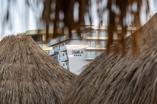 a building in the background with a straw roof at L&C Beach Home by Zora apartament,pe plaja in Mamaia Nord