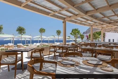 a restaurant with tables and chairs with the ocean in the background at Sandblu Resort in Kamari
