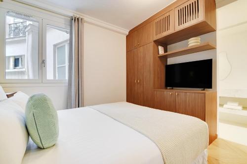 une chambre avec un lit blanc et une télévision dans l'établissement ONIRI - Serviced Apartment in Saint Germain, à Paris