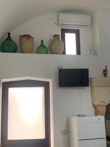 a kitchen with a shelf with vases and a television at La Casetta nel Vico in Andrano