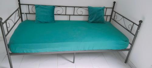 a bed with green sheets and two blue pillows at Appartement meublé neuf, près de Paris et Beauvais in Amblainville