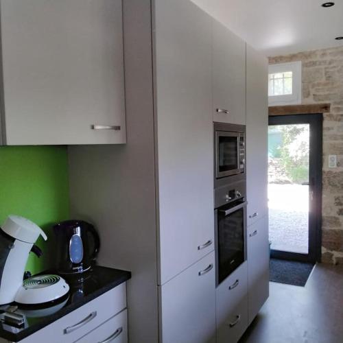 - une cuisine avec des placards blancs et un mur vert dans l'établissement Maison, à Nespouls