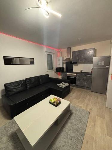 un salon avec un canapé noir et une cuisine dans l'établissement Appart Cosy, à Montfermeil