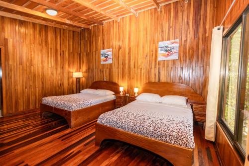 two beds in a room with wooden walls at Jaguarundi Jungle Lodge - Monteverde in Monteverde Costa Rica