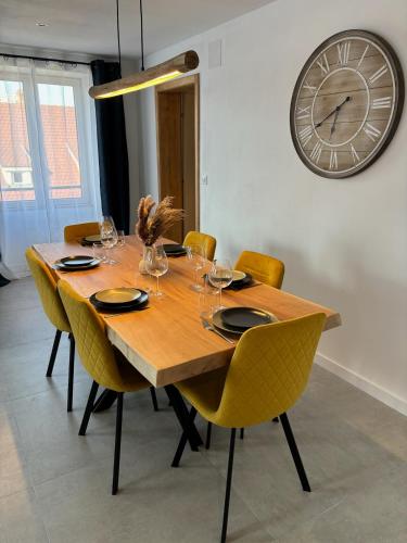 une table en bois avec des chaises et une horloge sur le mur dans l'établissement Gîte Eden classer 3 étoiles, à Colmar