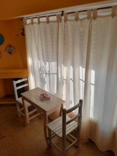 Una mesa y sillas junto a una ventana con cortinas blancas. en Alojamiento céntrico, en Puerto Madryn