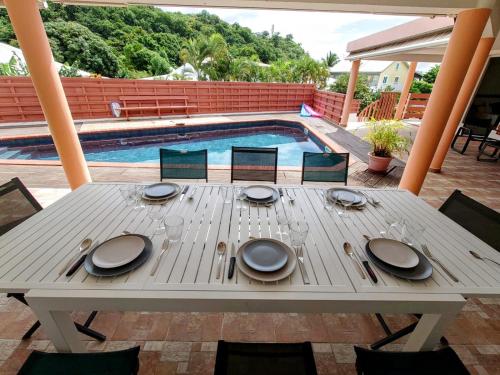a wooden table with plates on it next to a swimming pool at Villa Béliya in Le Carbet