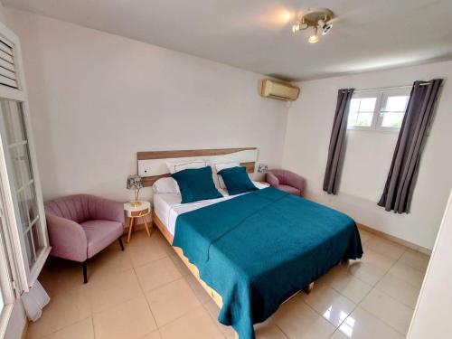 a bedroom with a bed and two pink chairs at Villa Béliya in Le Carbet