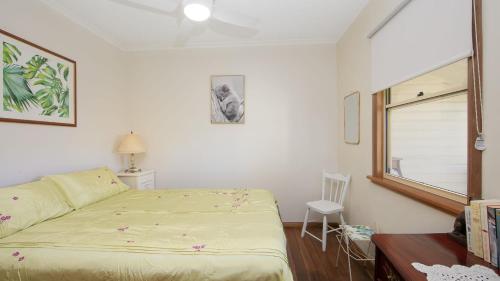 une chambre avec un lit, une fenêtre et une chaise dans l'établissement Cane Cutters Cottage, à Woombah