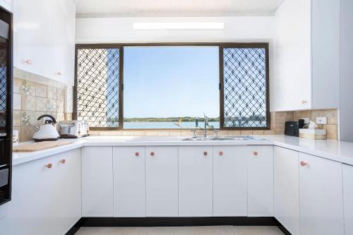 a kitchen with white cabinets and a window at River Front Escape, Short Walk to Ocean Street in Maroochydore