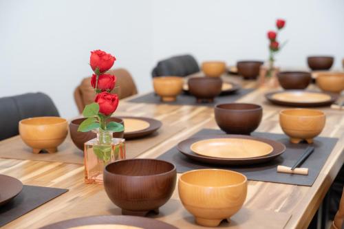 a long wooden table with brown bowls and a vase with a rose at Guest House 橘 関西空港直通,2階建て丸ごと貸切,難波,道頓堀まで2駅5分 in Osaka