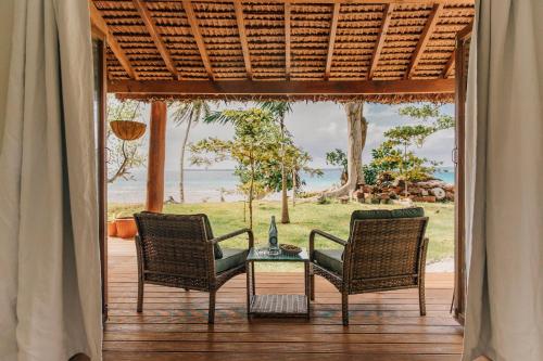 three chairs and a table on a porch with a view of the ocean at Aore Paradise - Near Santo, Vanuatu in Aore Island