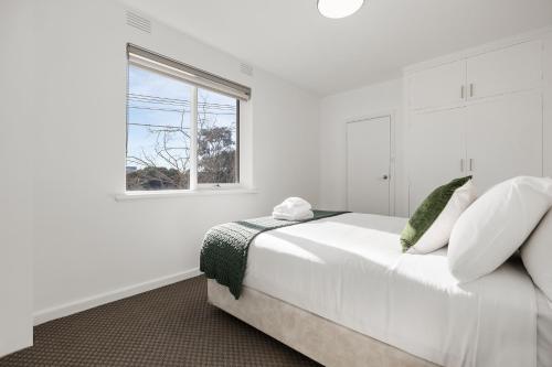 a white bedroom with a bed and a window at Windsor Apartments by Urban Rest in Melbourne