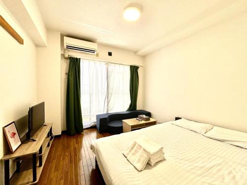 a bedroom with a bed and a television and a chair at Guest House Flora Otemachi/フローラ大手町 in Hiroshima