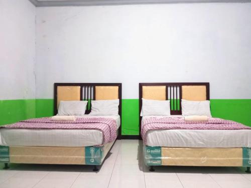 two beds sitting next to each other in a room at Puspa Tiara Syar'i Guci Mitra RedDoorz in Tuwel