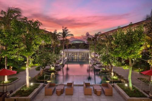 a resort pool with lounge chairs and trees at dusk at Hilton Garden Inn Bali Ngurah Rai Airport in Kuta