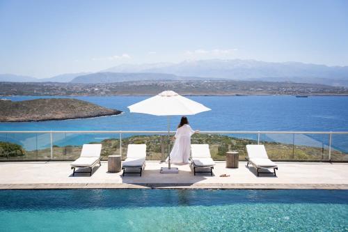 a woman standing next to a swimming pool with an umbrella at Seacrete villas in Chania