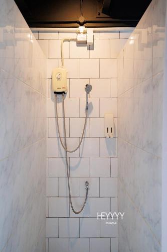 a shower with a hose in a white tiled bathroom at Heyyyy Bangkok in Bang Kapi