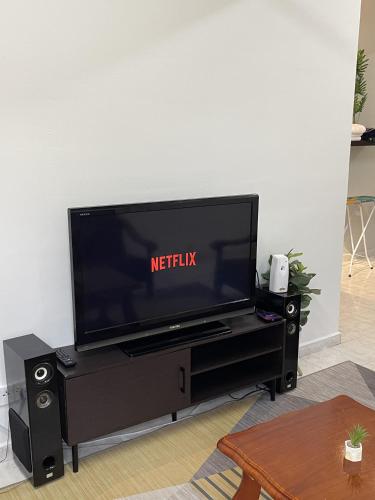 a flat screen tv on a black entertainment center at Peaceful Pines 4 ROOMS FULL AC & NETFLIX by EZYROOM MELAKA in Ayer Keroh